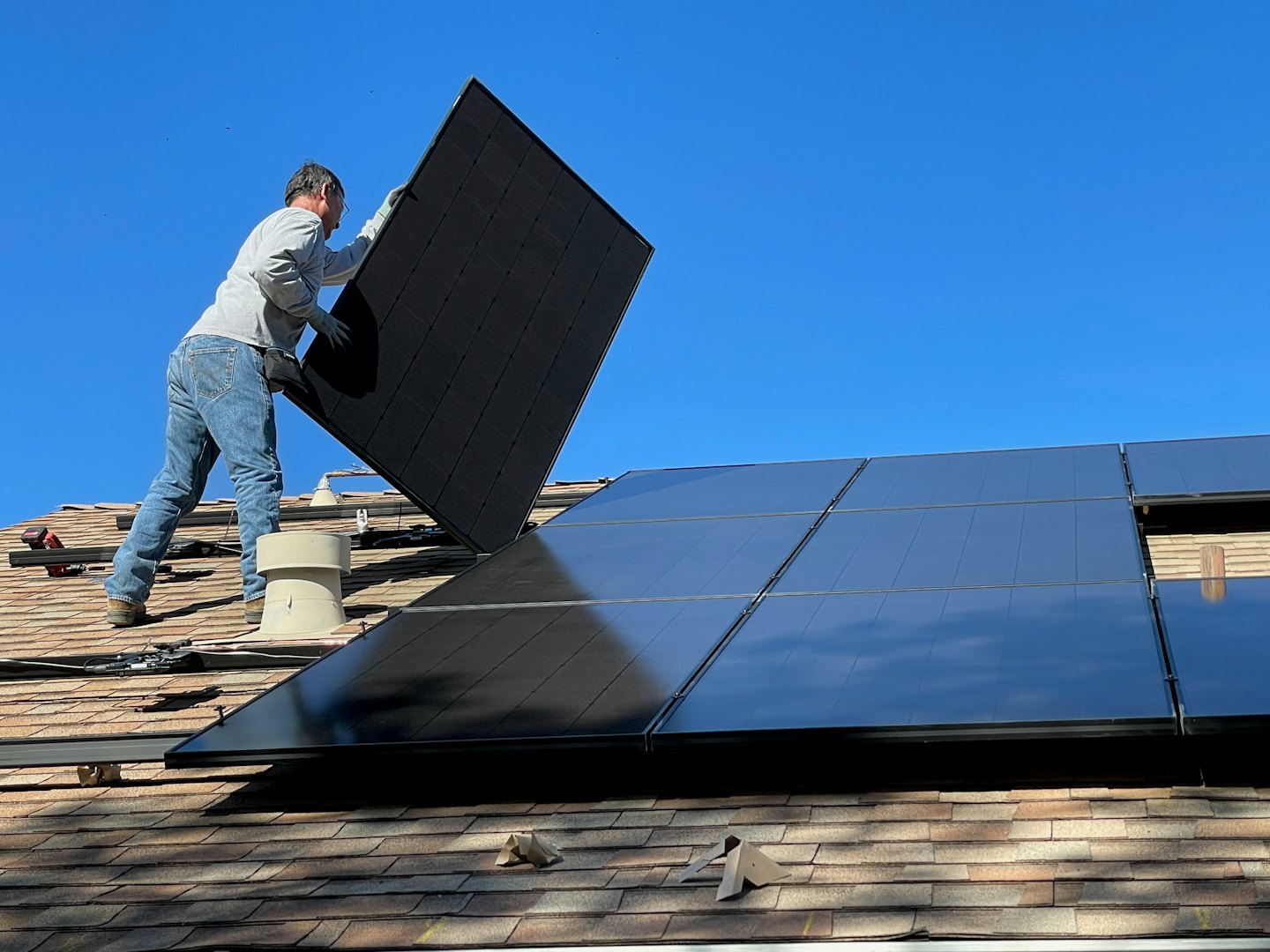 Técnico instala panel solar en tejado de tejas bajo cielo azul.
